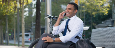 An image of a young businessman sitting on a parkbench and talking on his cellphone.